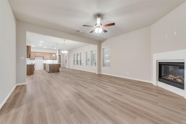 unfurnished living room with sink, ceiling fan with notable chandelier, and light wood-type flooring