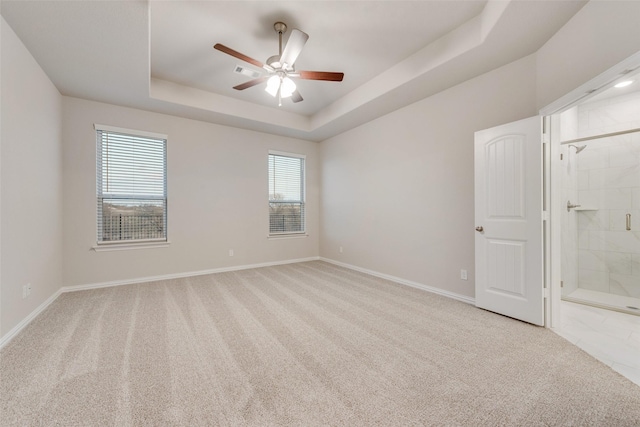 carpeted spare room with a raised ceiling and ceiling fan