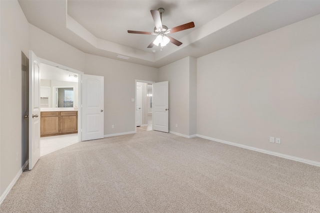 unfurnished bedroom featuring connected bathroom, a tray ceiling, light colored carpet, and ceiling fan