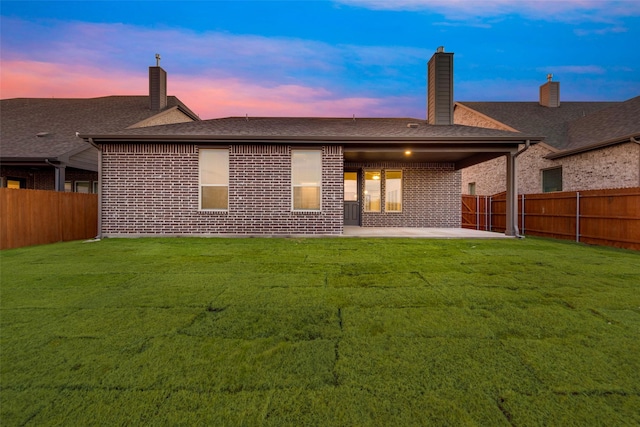 back house at dusk featuring a yard and a patio area