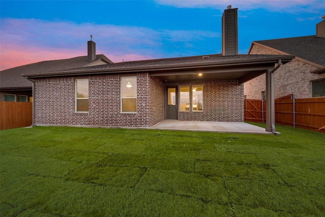 back house at dusk featuring a lawn and a patio