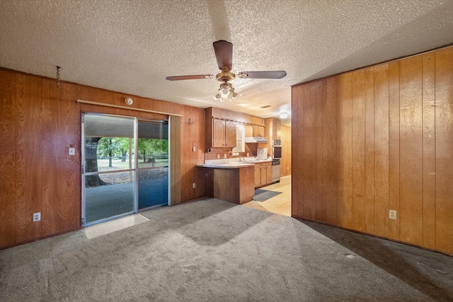 interior space with ceiling fan, a textured ceiling, wooden walls, and light carpet