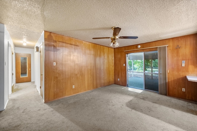 carpeted spare room with ceiling fan, a textured ceiling, and wood walls