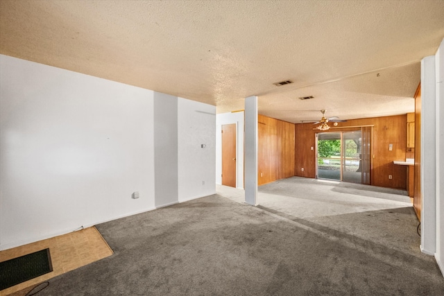 unfurnished living room featuring carpet floors, a textured ceiling, wooden walls, and ceiling fan