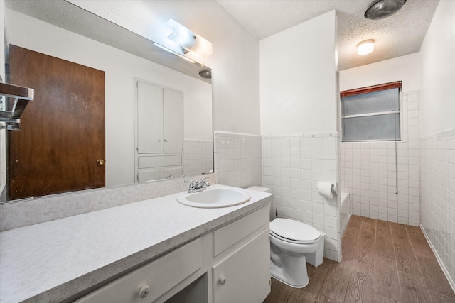 bathroom featuring vanity, toilet, a textured ceiling, tile walls, and hardwood / wood-style floors