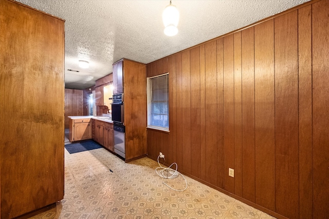 kitchen featuring a textured ceiling, wooden walls, and decorative light fixtures