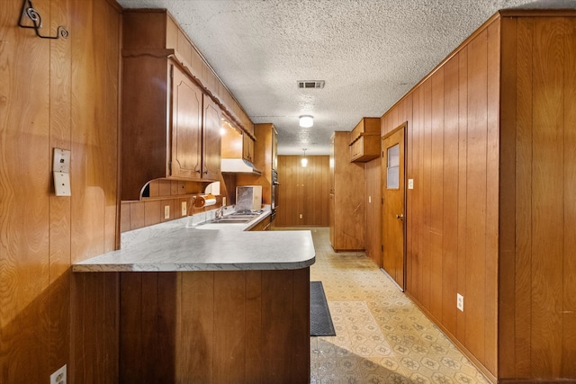 kitchen with a textured ceiling, kitchen peninsula, wooden walls, and oven