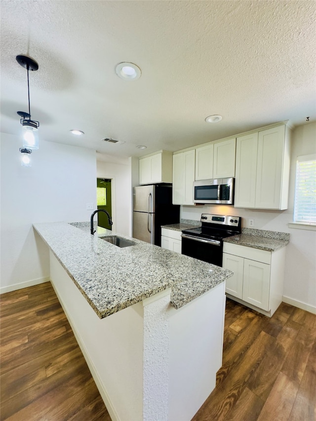 kitchen with appliances with stainless steel finishes, light stone counters, kitchen peninsula, dark hardwood / wood-style floors, and sink