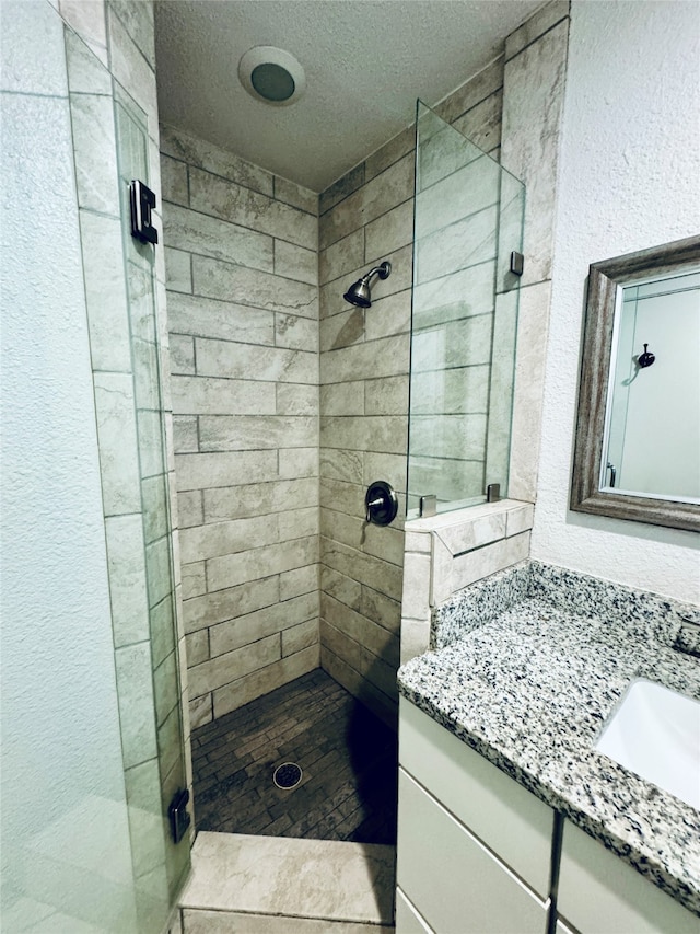 bathroom with a tile shower, a textured ceiling, and vanity