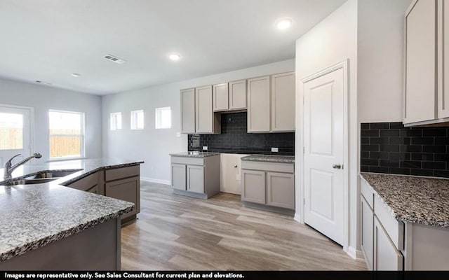 kitchen with light wood-type flooring, gray cabinetry, decorative backsplash, and sink