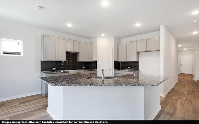 kitchen with decorative backsplash, light wood-type flooring, an island with sink, and sink