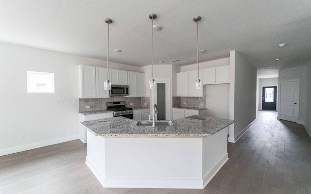 kitchen with a center island with sink, appliances with stainless steel finishes, light stone counters, white cabinetry, and a sink