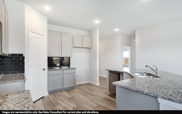 kitchen with light stone countertops, light hardwood / wood-style floors, decorative backsplash, and sink