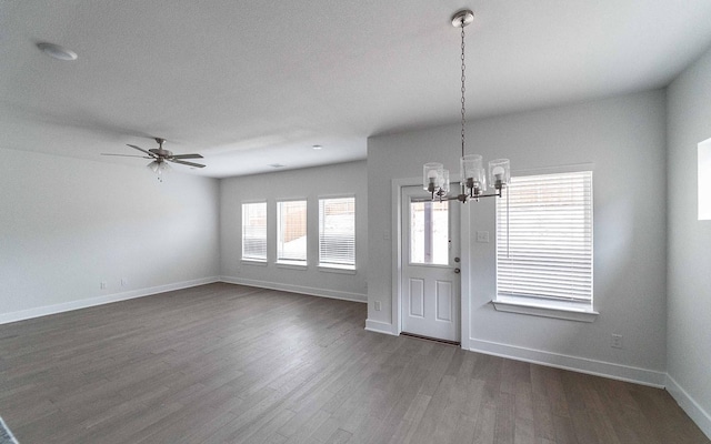 unfurnished dining area featuring ceiling fan with notable chandelier, dark wood-type flooring, and baseboards