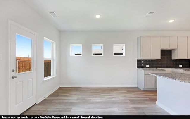 kitchen featuring white cabinets, light hardwood / wood-style flooring, light stone countertops, and decorative backsplash