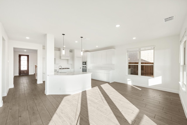 kitchen with pendant lighting, sink, white cabinetry, and an island with sink