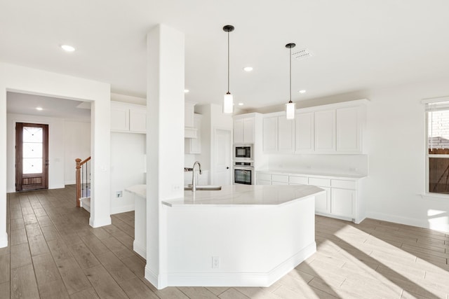 kitchen with stainless steel oven, built in microwave, sink, decorative light fixtures, and white cabinetry