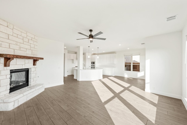 unfurnished living room with hardwood / wood-style flooring, ceiling fan, a stone fireplace, and sink