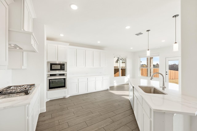 kitchen with pendant lighting, white cabinets, sink, light stone countertops, and appliances with stainless steel finishes