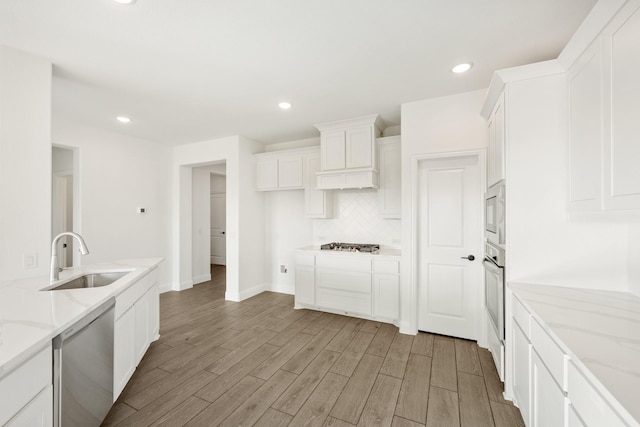 kitchen with decorative backsplash, appliances with stainless steel finishes, light stone countertops, sink, and white cabinets