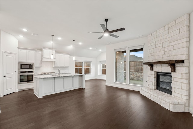 kitchen featuring white cabinetry, black microwave, a center island with sink, pendant lighting, and oven