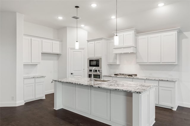 kitchen with appliances with stainless steel finishes, decorative light fixtures, an island with sink, white cabinets, and light stone countertops