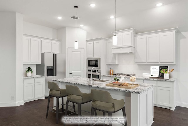 kitchen with appliances with stainless steel finishes, dark hardwood / wood-style floors, pendant lighting, white cabinets, and a center island with sink