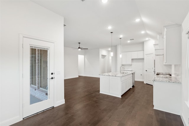 kitchen with dark hardwood / wood-style floors, pendant lighting, white cabinetry, a kitchen island with sink, and light stone countertops