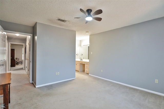 unfurnished bedroom featuring ceiling fan, sink, ensuite bathroom, a textured ceiling, and light carpet