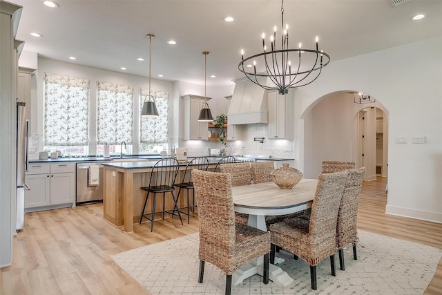 dining space featuring an inviting chandelier, light wood-type flooring, recessed lighting, and arched walkways