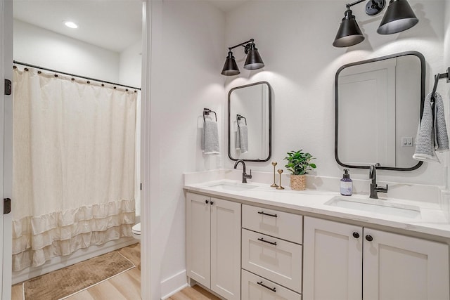 full bath with toilet, double vanity, a sink, and wood finished floors
