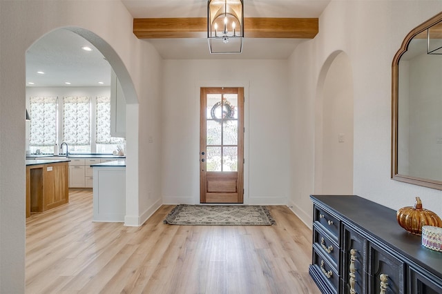 entrance foyer with a notable chandelier, light hardwood / wood-style floors, beam ceiling, and sink