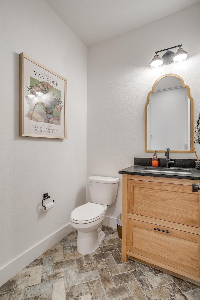 bathroom with baseboards, stone finish flooring, toilet, and vanity