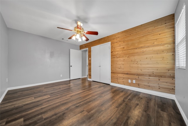 interior space with wood walls, dark hardwood / wood-style floors, and ceiling fan