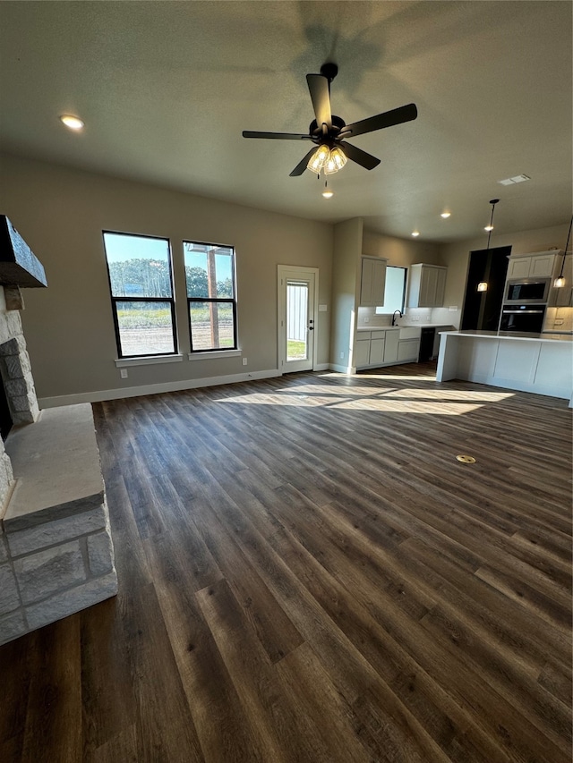 unfurnished living room featuring a textured ceiling, dark wood-type flooring, sink, a fireplace, and ceiling fan