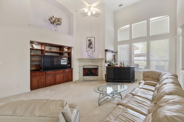 carpeted living room featuring a premium fireplace, a high ceiling, and ceiling fan