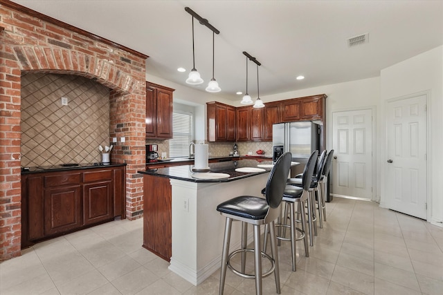 kitchen with light tile patterned floors, a kitchen island, brick wall, decorative light fixtures, and stainless steel refrigerator with ice dispenser