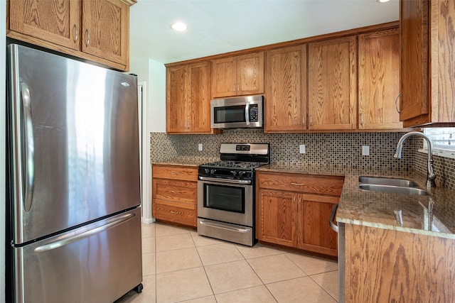 kitchen featuring light stone counters, appliances with stainless steel finishes, light tile patterned floors, decorative backsplash, and sink