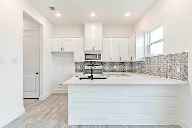 kitchen with light hardwood / wood-style floors, kitchen peninsula, white cabinetry, and sink