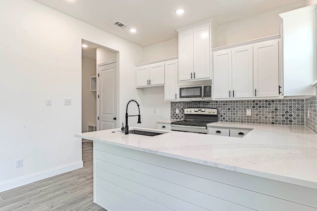 kitchen featuring appliances with stainless steel finishes, light stone counters, white cabinets, kitchen peninsula, and sink