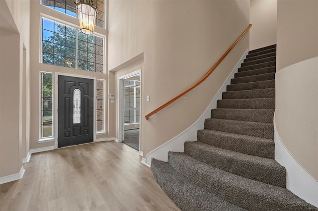 foyer featuring an inviting chandelier, a towering ceiling, and light hardwood / wood-style flooring