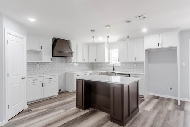 kitchen featuring premium range hood, decorative light fixtures, white cabinetry, a center island, and light hardwood / wood-style floors