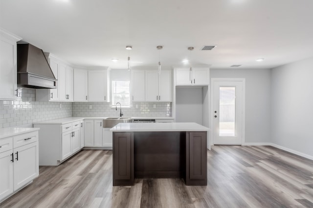 kitchen with sink, light hardwood / wood-style flooring, white cabinetry, custom range hood, and a center island