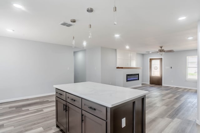 kitchen featuring ceiling fan, hanging light fixtures, light hardwood / wood-style flooring, a large fireplace, and light stone countertops