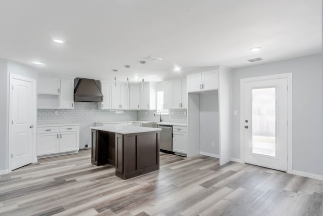 kitchen with dishwasher, white cabinetry, a kitchen island, custom exhaust hood, and decorative light fixtures