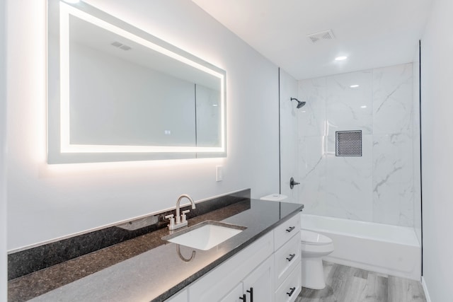 full bathroom featuring wood-type flooring, tiled shower / bath, vanity, and toilet