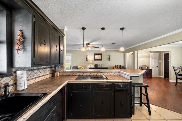 kitchen with light hardwood / wood-style floors, a breakfast bar, kitchen peninsula, ceiling fan, and ornamental molding