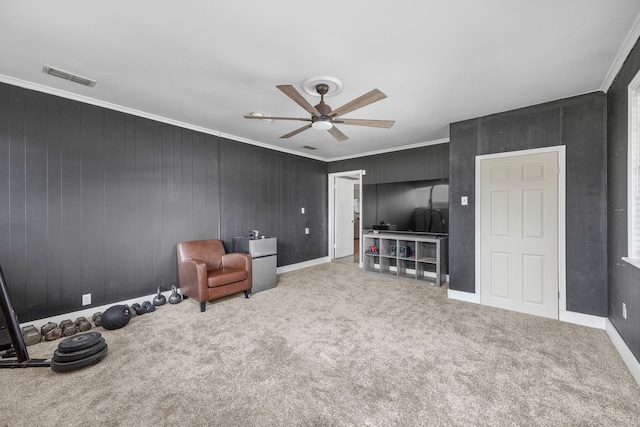 sitting room featuring ceiling fan, carpet flooring, wood walls, and ornamental molding