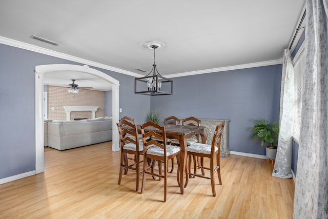 dining area featuring ceiling fan with notable chandelier, a fireplace, ornamental molding, and light hardwood / wood-style flooring