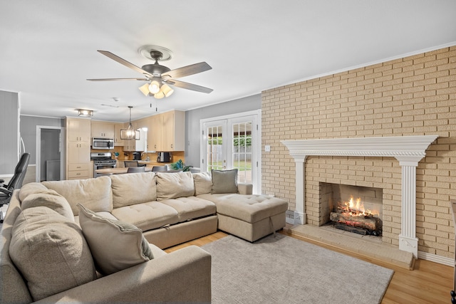 living room with light wood-type flooring, a brick fireplace, ornamental molding, ceiling fan, and brick wall